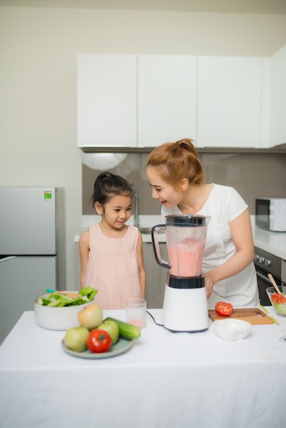 Mother assisting daughter to prepare juice in kitchen at home