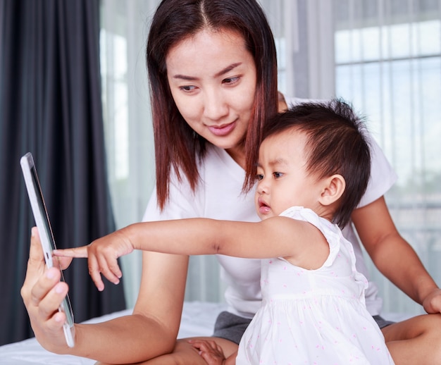 Mother and baby are looking to play and read tablet computer on bed