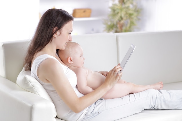 Mother and baby are looking to play and read tablet computer on the couch at home