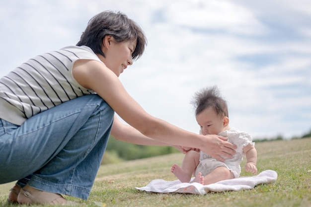 A mother and baby are sitting on a blanket in a park.