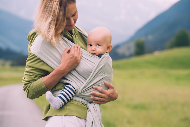 Madre e bambino sulla natura all'aperto baby in wrap carrier donna che trasporta piccolo bambino in fascia per bambini