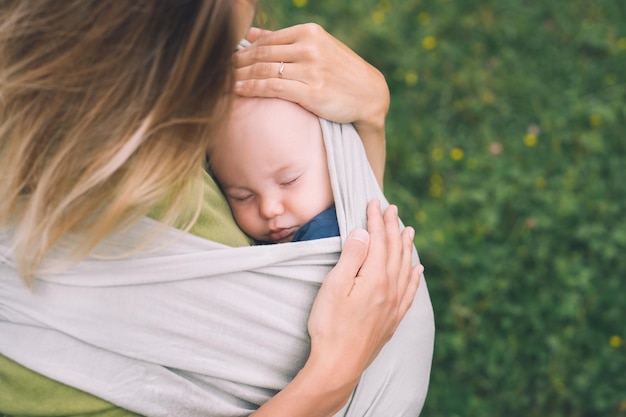 Madre e bambino sulla natura all'aperto baby in wrap carrier donna che trasporta piccolo bambino in fascia per bambini