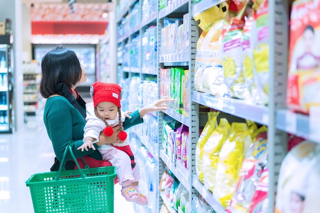 スーパーマーケットでの母親と赤ちゃんの買い物タイの女性は娘を持っています