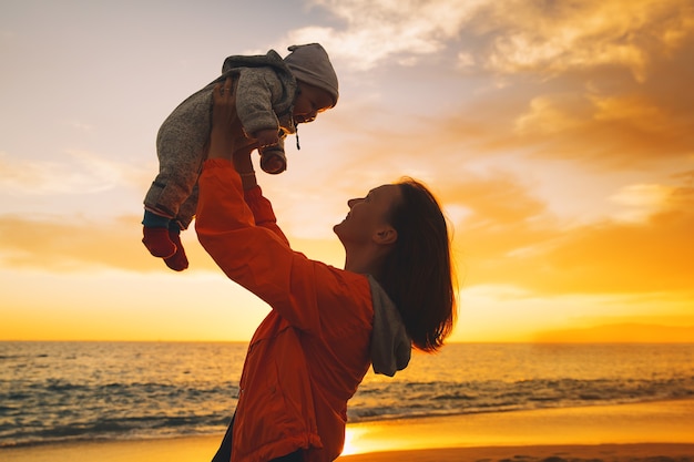 Sagome di madre e bambino al tramonto sulla spiaggia oceano in estate sfondo famiglia felice