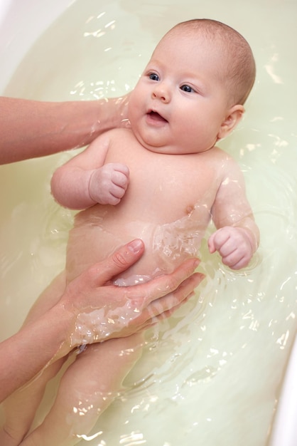 Mother bathes her baby in a white small plastic tub