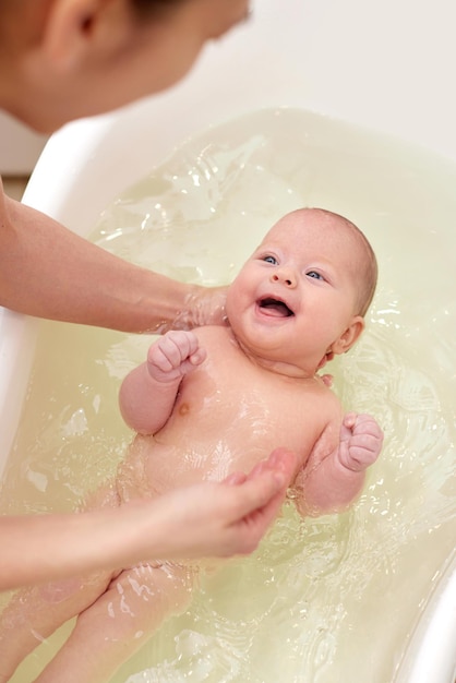 Mother bathes her baby in a white small plastic tub