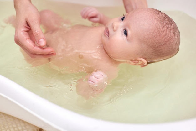 Mother bathes her baby in a white small plastic tub