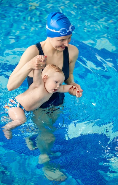 Mother and boy at baby swimming lesson doing exercises in water Baby walking in water with mother help and hands up