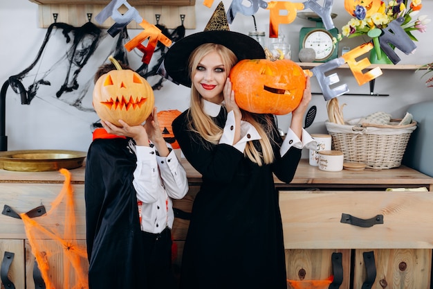 Foto madre e ragazzo in piedi in costume tenendo una zucca. il ragazzo nasconde il viso