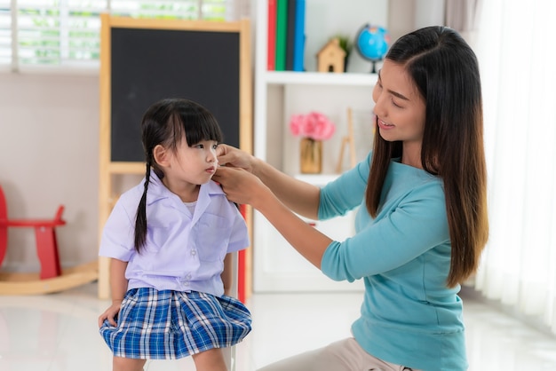 mother Braiding her daughters hair sitting on chair, smiling single mom sister helping child girl with hairstyle