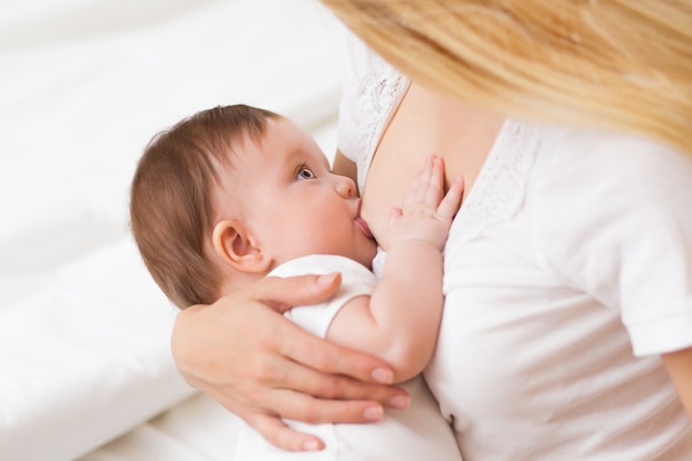 Mother breast feeding and hugging her baby.Young mother feeding breast her babyboy at home in white room. Mom breastfeeding her child whith breast milk