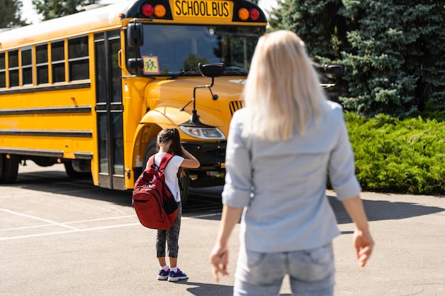 Мать приводит дочь в школу возле школьного автобуса. обратно в школу