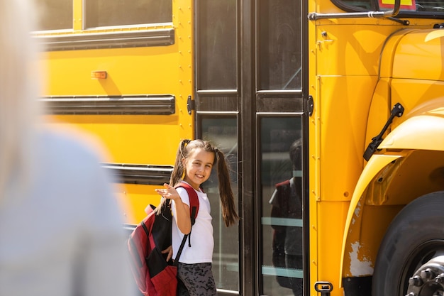 Mother brings her daughter to school near the school bus. back to school