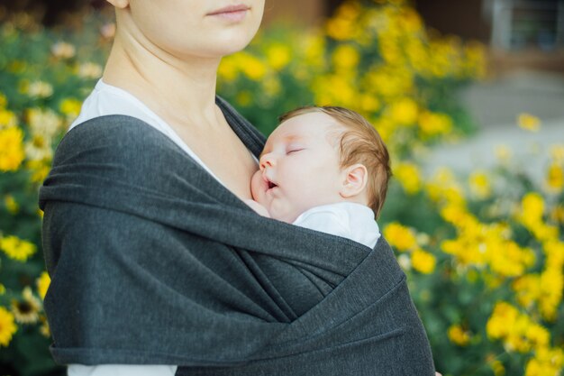 Mother carrying sleeping baby in sling, attachment parenting concept.