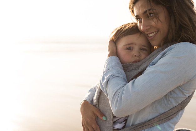 Photo mother carrying son while standing at beach