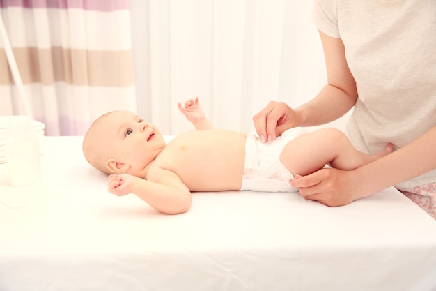 Mother changing diaper to little baby in room