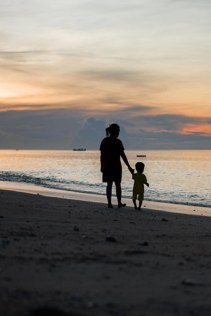 A mother and child are walking on the beach at sunset.