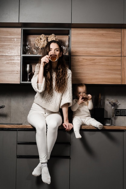 Mother and child daughter are drinking cup of tea on the kitchen Maternity Mon and her kid spend time at home together