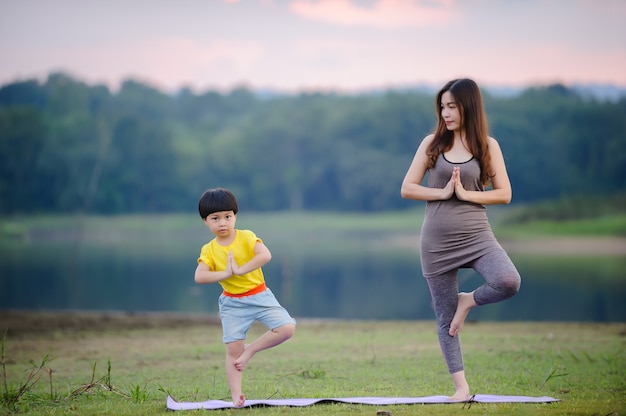 Madre e bambino che fanno esercizi di yoga sull'erba al parco prima del tramonto in estate.