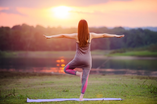 Mother and child doing yoga exercises on grass at the park befor sunset in summer.