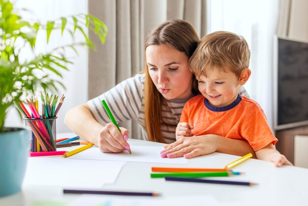 Mother and child drawing with pencils sitting at the desk at home Happy family