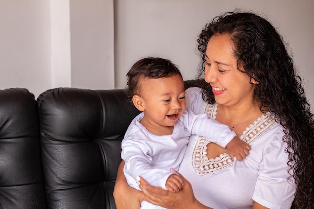 Mother and child dressed in white sitting on a sofa Smiling and happy baby next to his mother