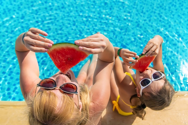 Mother and child eat watermelon by the pool