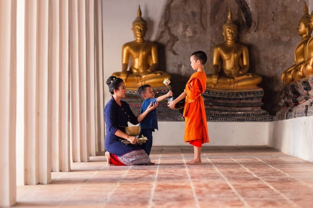 母と子の家族タイ仏教徒は、タイのアユタヤにあるワットプッタイサワン寺院で僧侶と一緒に功徳を上げている初心者に施しをしています。