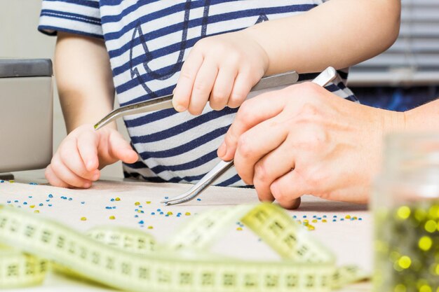 母と子は手工芸品の創造性のために生地の職場でビーズのパターンを作ります