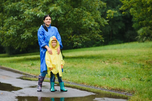 母と子が雨の中で遊んで、ブーツとレインコートを着ている