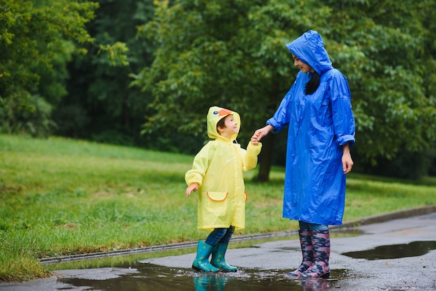 母と子が雨の中で遊んで、ブーツとレインコートを着ている