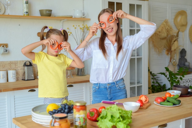 Madre e figlio che preparano cibo sano e si divertono tengono un peperone davanti ai loro occhi