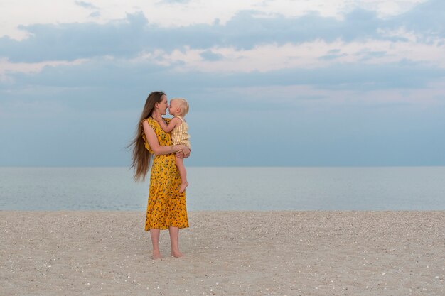 Mother and child on sandy beach on sea and sky background. Maternal care and love. Seaside holiday with baby.