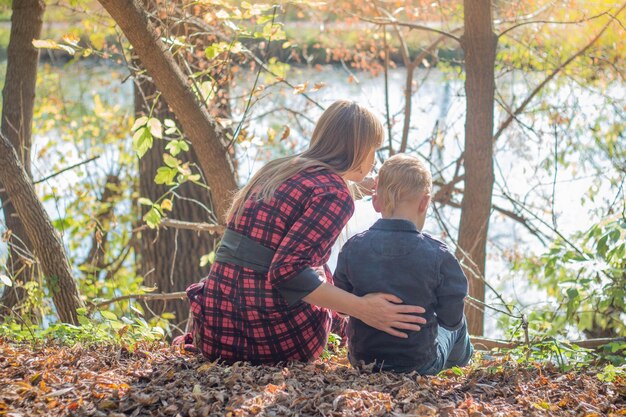 A mother and child sit on the ground in front of a river.