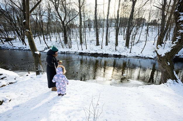 Madre e bambino che camminano in una giornata invernale gelida e soleggiata nel parco vicino al fiume con anatre e uccelli