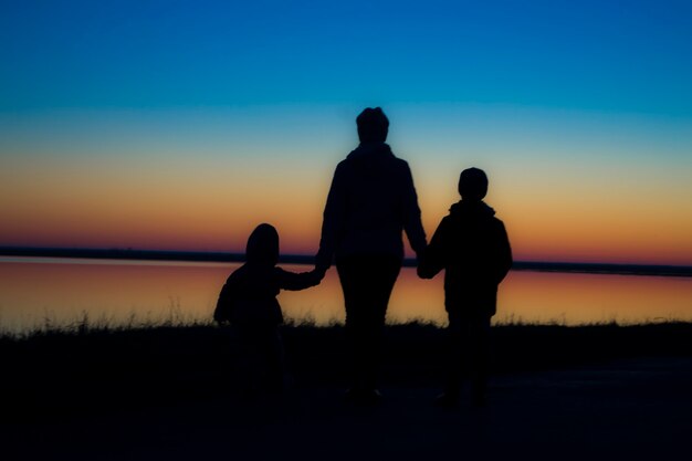 Mother and children hold hands in the background of the sunset