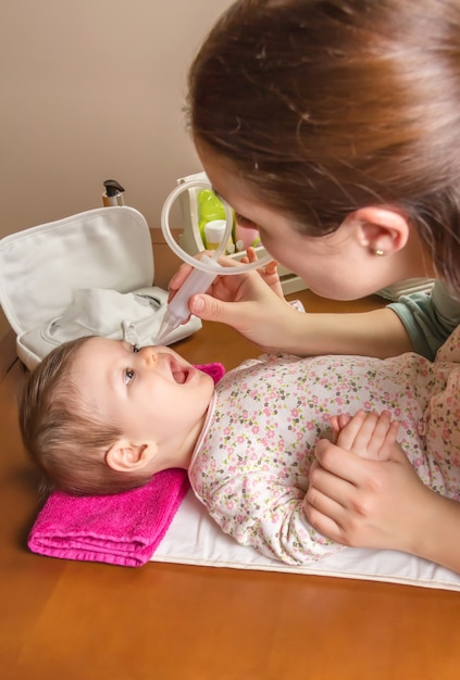 鼻吸引器で愛らしい赤ちゃんの粘液カタルを掃除する母親