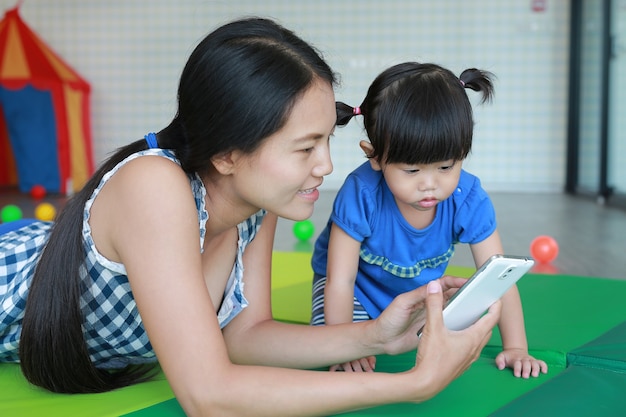 母親とかわいいアジアの赤ちゃんの女の子がスマートフォンをプレイし、キッドルームで寝る