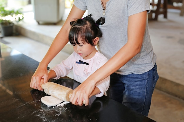 Mother and Cute little girl using Wooden rolling pin on Dough for pizza