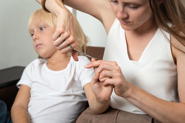 Mother cutting nails on hands of her son sitting on the couch Childcare