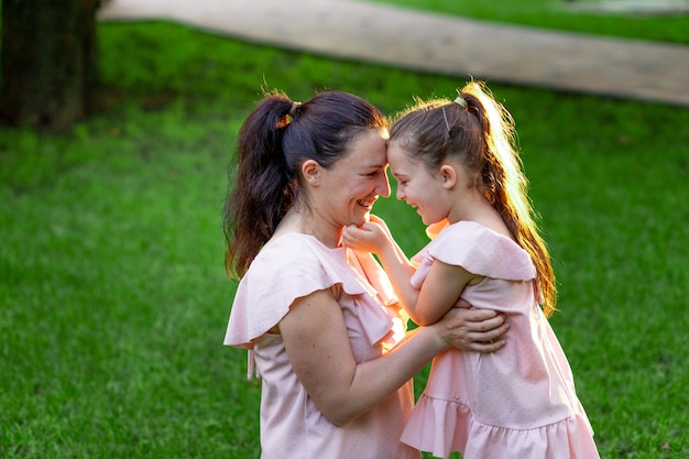 Madre e figlia di 5-6 anni si siedono nel parco sull'erba d'estate e ridono, conversando madre-figlia