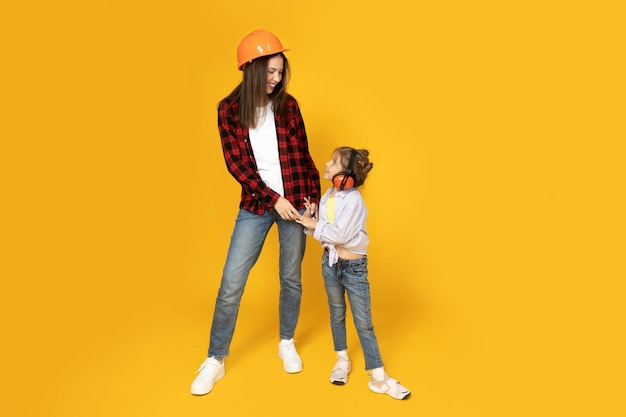 Mother and daughter in accessories for construction on a yellow background