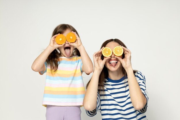 Photo mother and daughter are joking with oranges instead of eyes on a gray background