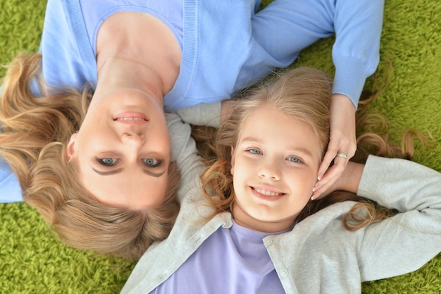 Mother and daughter are lying on a green carpet