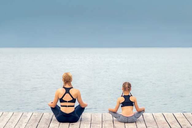 Mother and daughter are meditating by the sea at pier