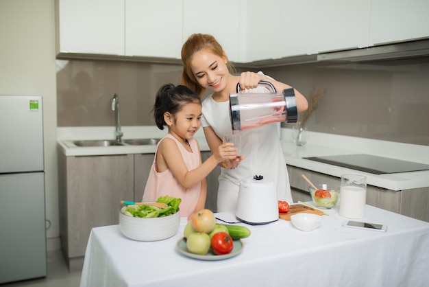Mother and Daughter are preparing the salad in blender Menu tasty smoothie and ingredients on table at home
