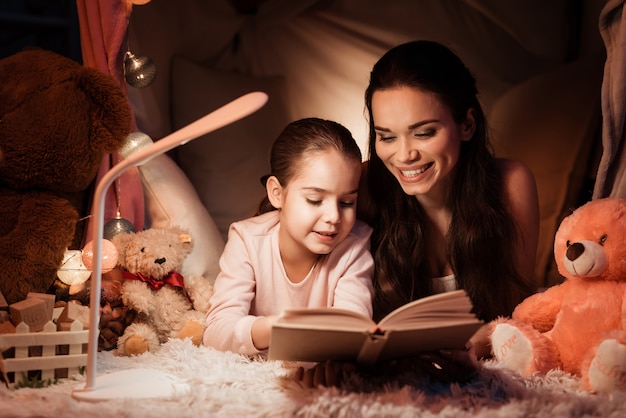 Mother and daughter are reading book in house.