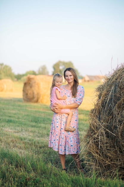 A mother and daughter are standing in a field with hay bales in the background