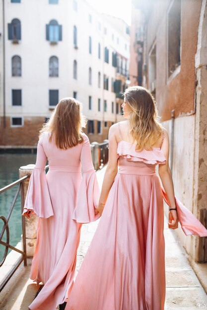 Mother and daughter are walking in sunny Venice in soft pink dresses Concept of active lifestyle