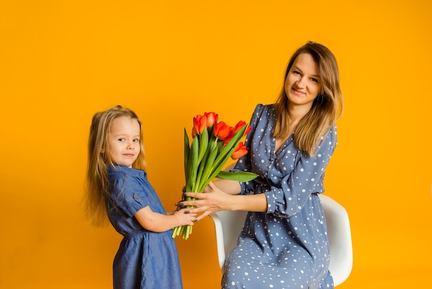 Mother and daughter in blue dresses with a bouquet of red tulips on a yellow wall
